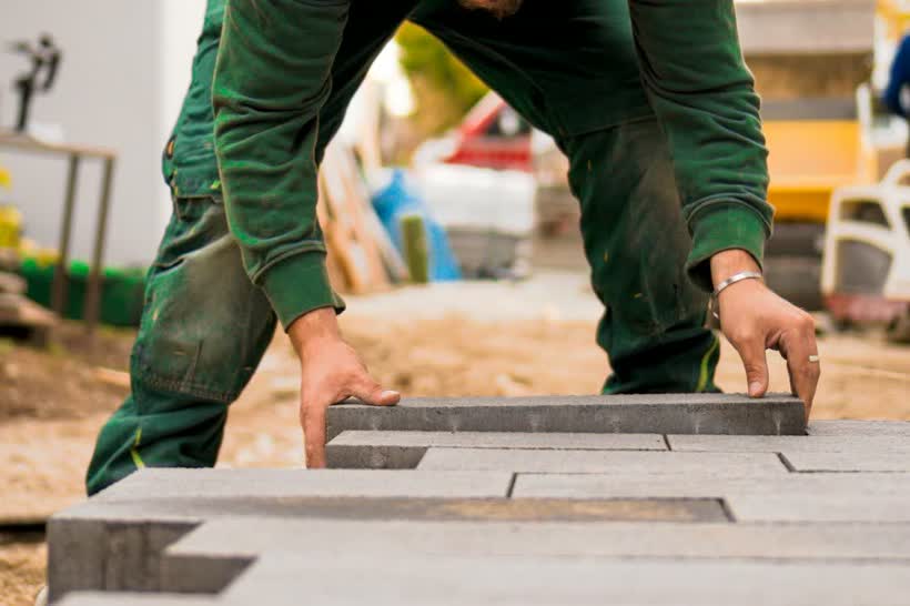Arbeiter setzt eine Betonplatte in das Pflasterbett